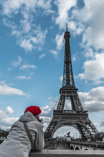 Молодая туристка в парижской красной шляпе смотрит на Эйфелеву башню со стороны Сены
 - Фото, изображение