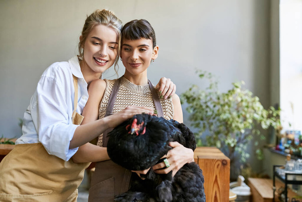 Dos mujeres en tierno abrazo con la gallina en un estudio de arte. - Foto, imagen