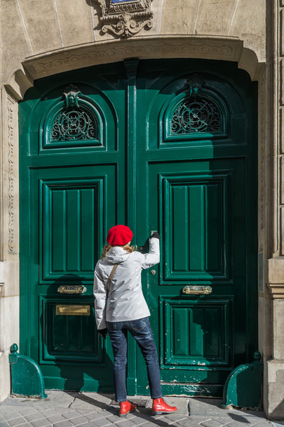 Молода мила жінка з червоним капелюхом і взуттям, стукає в старовинні зелені дерев'яні двері
 - Фото, зображення