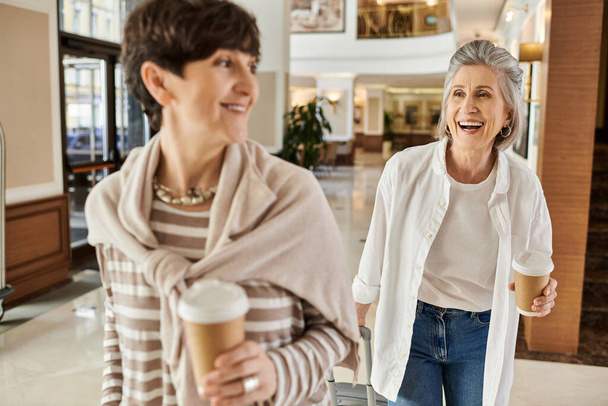 Zwei Frauen genießen einen Spaziergang durch ein Einkaufszentrum, während sie Kaffeetassen in der Hand halten. - Foto, Bild