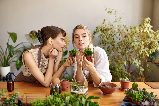 Обнимая артистизм, две женщины сидят за столом в окружении пышных зеленых растений. - Фото, изображение