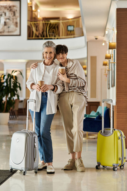 Senior λεσβιακό ζευγάρι, μια αγάπη ανώτερος λεσβιακό ζευγάρι, σταθεί σε ένα λόμπι του ξενοδοχείου με αποσκευές. - Φωτογραφία, εικόνα