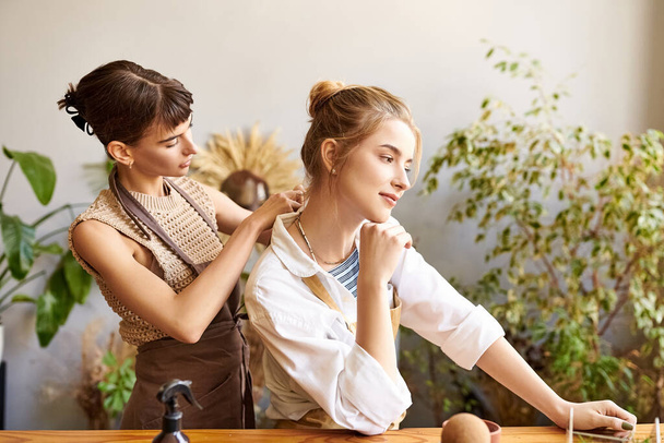 Две женщины, стоящие за столом с растением, демонстрируют воспитательную и художественную связь. - Фото, изображение