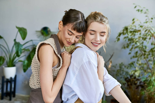 Δύο γυναίκες μοιράζονται μια εγκάρδια αγκαλιά σε ένα χώρο γεμάτο τέχνη. - Φωτογραφία, εικόνα
