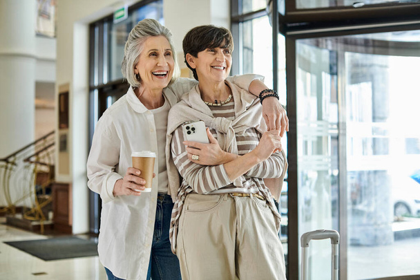 Deux lesbiennes âgées se tiennent devant un hôtel, rayonnant d'élégance et d'amour. - Photo, image