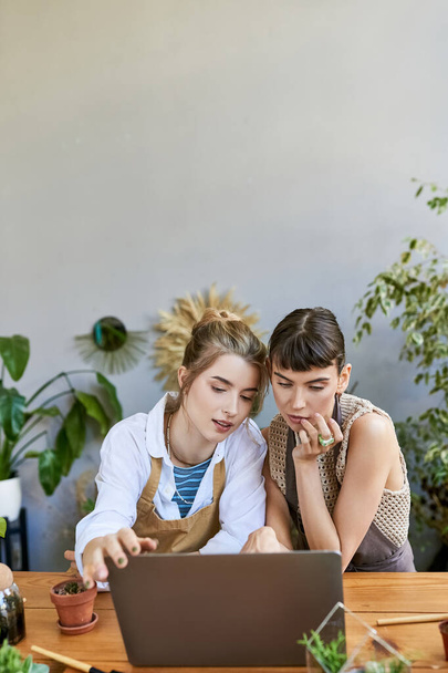 Un couple de lesbiennes amoureux plongé dans leur art, collaborant sur un ordinateur portable à une table. - Photo, image