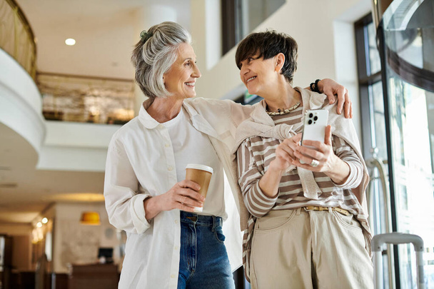 Twee vrouwen, een senior lesbisch paar, naast elkaar staan met koffiebekers. - Foto, afbeelding
