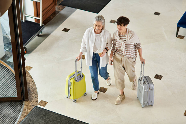 Αγαπώντας ηλικιωμένες λεσβίες ζευγάρι που περπατούν στο διάδρομο του ξενοδοχείου με αποσκευές. - Φωτογραφία, εικόνα