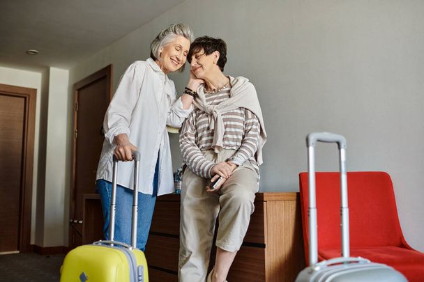 een senior lesbisch paar staan samen met een koffer in een hotel. - Foto, afbeelding