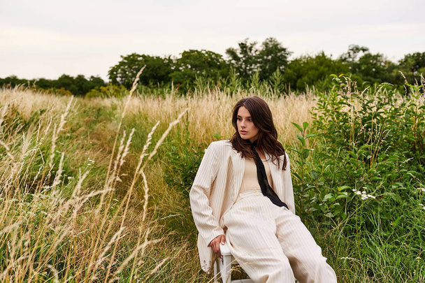 Красива молода жінка в білому вбранні сидить мирно на стільці в полі, замочуючи в літній бриз. - Фото, зображення