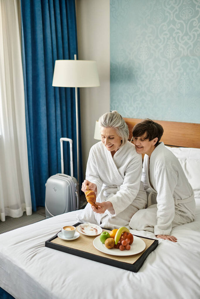 Senior λεσβιακό ζευγάρι μοιράζονται μια τρυφερή στιγμή σε ένα άνετο κρεβάτι. - Φωτογραφία, εικόνα