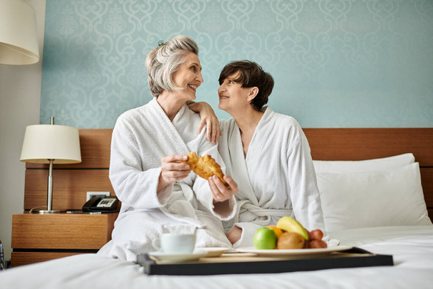 Senior lesbian couple enjoying a tender moment on top of a cozy bed. - Photo, Image
