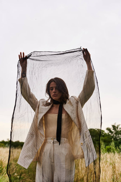 Eine schöne junge Frau in weißem Gewand steht auf einem Feld, die Hände in der Luft und umarmt die Freiheit und Schönheit der Natur.. - Foto, Bild