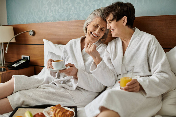 Dwie starsze kobiety siedzą blisko na łóżku, ucieleśniając miłość i spokój. - Zdjęcie, obraz