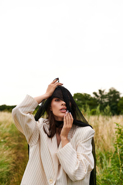 Eine schöne junge Frau in weißem Gewand steht mit einem Schleier, der in der Sommerbrise in einem ruhigen Feld weht. - Foto, Bild
