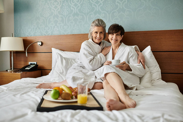 Tendre couple lesbienne senior assis ensemble sur le bord d'un lit avec amour et confort. - Photo, image