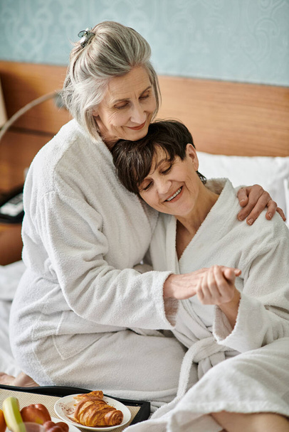 czuły moment między kochającą starszą parą lesbijek, przytulającą się w łóżku. - Zdjęcie, obraz