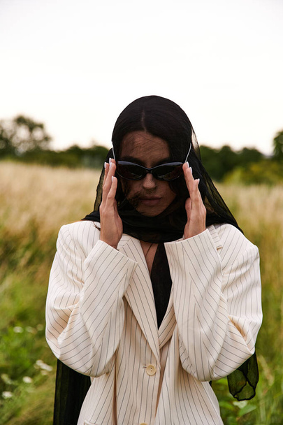 Eine stilvolle Frau in Anzug und Sonnenbrille steht selbstbewusst in einem weiten Feld und verkörpert Anmut und Raffinesse in der Natur. - Foto, Bild