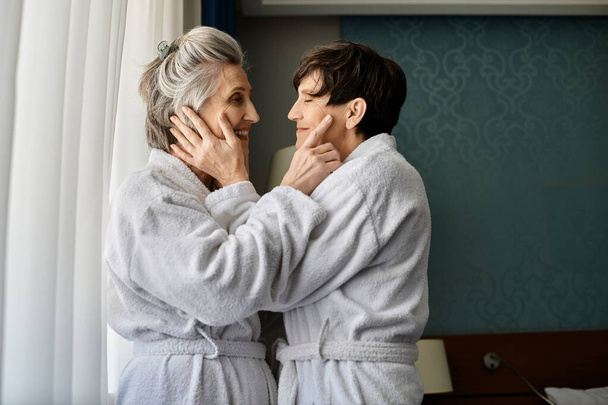 senioren lesbisch paar in badjassen bewonderen het uitzicht door een raam. - Foto, afbeelding