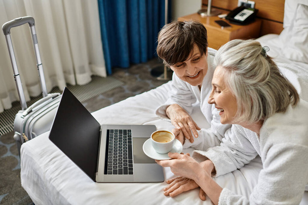 Una coppia lesbica anziana seduta su un letto, usando un computer portatile. - Foto, immagini