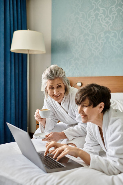 Ein älteres lesbisches Paar liegt friedlich im Bett, in einen Laptop vertieft. - Foto, Bild