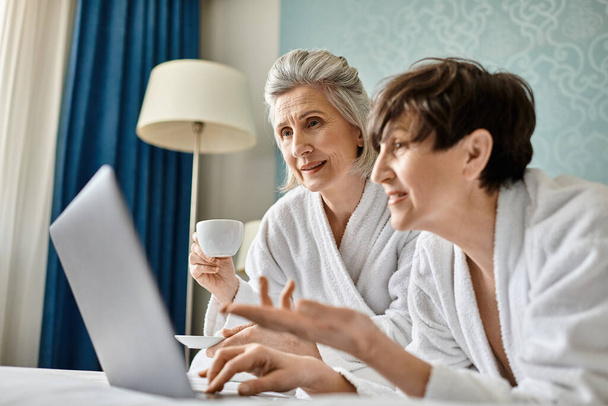 Una amante pareja de lesbianas mayores se sienta tiernamente en una cama, compartiendo un momento de conexión. - Foto, imagen