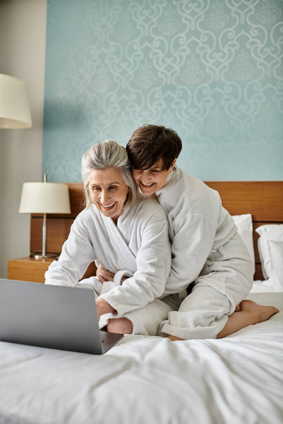 Starsza lesbijka para pochłonięta laptopem na łóżku. - Zdjęcie, obraz
