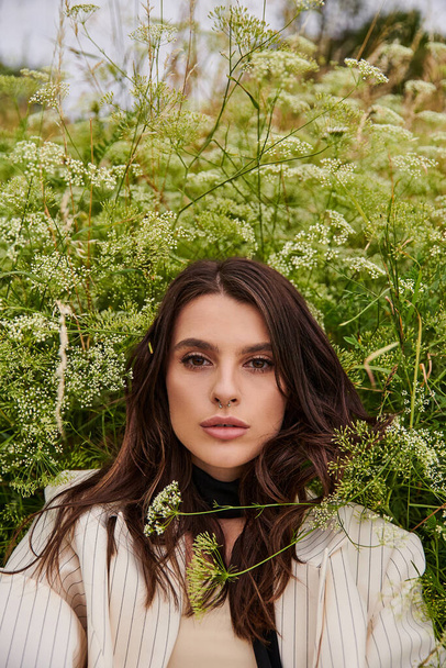 Eine schöne junge Frau in weißem Gewand steht anmutig auf einem Feld aus hohem Gras und umarmt die sanfte Sommerbrise. - Foto, Bild
