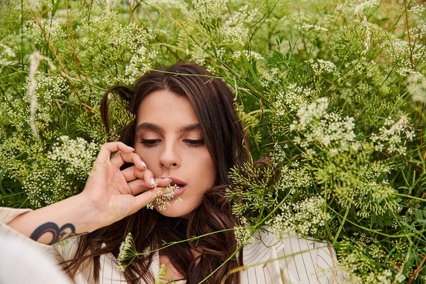 A young woman in white attire relaxes in a field of flowers, enjoying the summer breeze. - Photo, Image