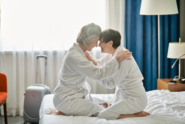 Een teder moment tussen een senior lesbisch paar zittend op een bed. - Foto, afbeelding
