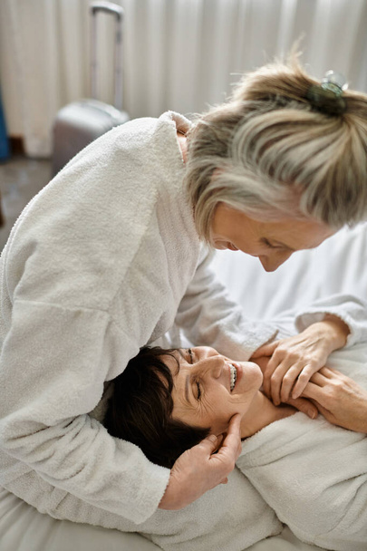 Czułe starsze lesbijki para w łóżku, jedna kobieta dotyka innych twarz z miłością. - Zdjęcie, obraz