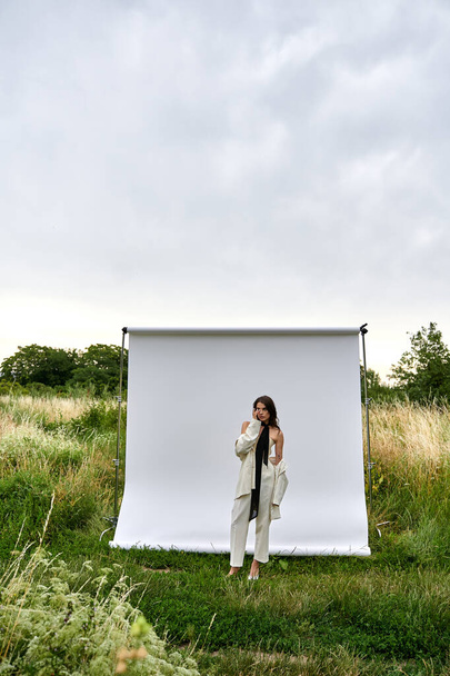 Eine junge Frau steht anmutig vor einer weißen Leinwand und verkörpert ein Gefühl von Eleganz und Gelassenheit in einer natürlichen Umgebung. - Foto, Bild