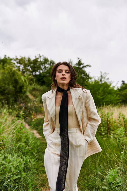 A stylish woman clad in a suit and tie stands confidently in a sunlit field, embracing the beauty of nature around her. - Photo, Image