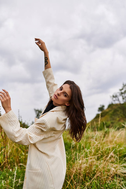 Een mooie jonge vrouw in witte kleding staat in een veld, genietend van de zomerbries. - Foto, afbeelding