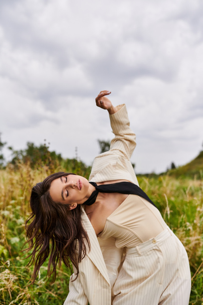 Een mooie jonge vrouw in een wit pak en zwarte stropdas genietend van de zomerbries in een veld. - Foto, afbeelding