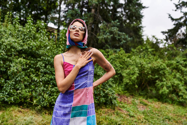 Een bruisende jonge vrouw draagt een kleurrijke handdoek staat sierlijk in een zonovergoten veld, belichaamt vreugde en schoonheid in de natuur. - Foto, afbeelding