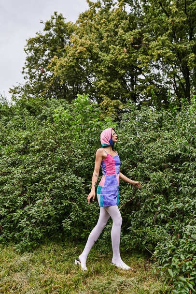 Uma jovem mulher em um vestido colorido e cachecol cabeça, abraçando a brisa de verão na natureza. - Foto, Imagem