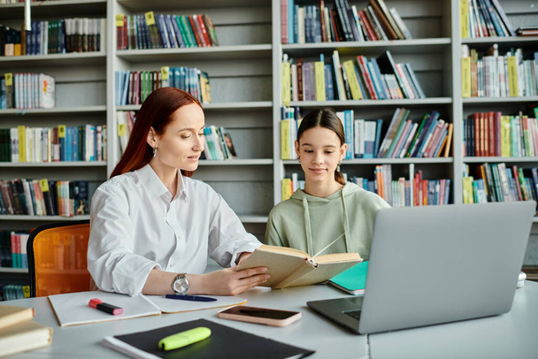 een tutor en een tienerstudent, met een laptop betrokken bij naschoolse lessen aan een bibliotheektafel. - Foto, afbeelding