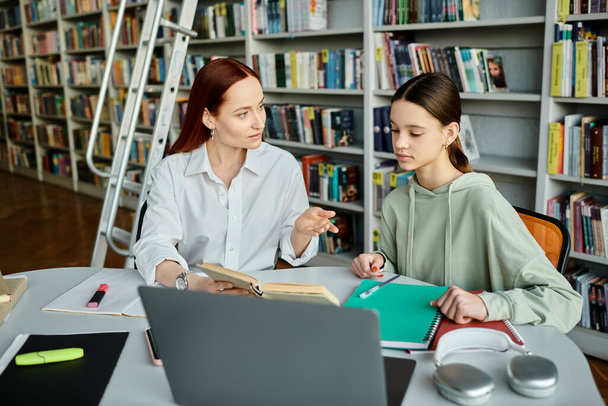 Un tutor dai capelli rossi che fornisce lezioni post-scolastiche a un'adolescente in una biblioteca, utilizzando un computer portatile per l'educazione moderna. - Foto, immagini