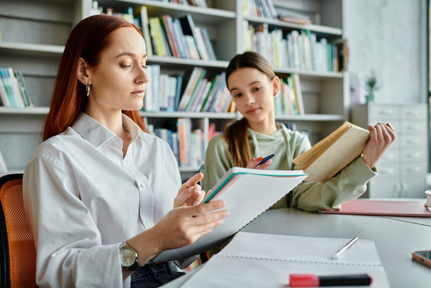 Un tutor rossa e una ragazza adolescente impegnati in lezioni post-scuola utilizzando un computer portatile in un ambiente biblioteca. - Foto, immagini