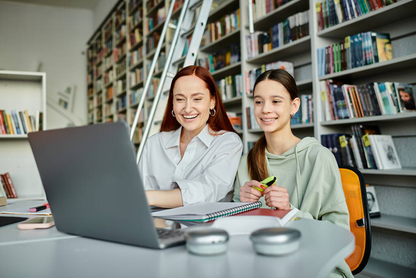 Redhead Tutor unterrichtet ein Teenager-Mädchen an einem Bibliothekstisch mit Laptops und engagiert sich im After-School-Unterricht. - Foto, Bild