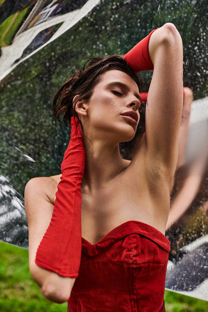 Uma jovem mulher em um vestido vermelho impressionante e luvas longas, apreciando a brisa de verão na natureza. - Foto, Imagem