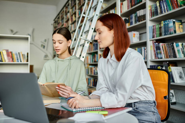 Egy vörös hajú oktató és egy tinédzser lány, akik élénk iskola utáni leckéket tartanak egy könyvtárban, egy laptop képernyőre koncentrálva.. - Fotó, kép
