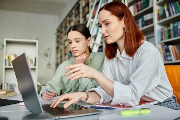 Redhead Tutor und Teenager Mädchen engagiert sich nach dem Schulunterricht, Verwendung eines Laptops für moderne Bildung in einer Bibliothek Einstellung. - Foto, Bild