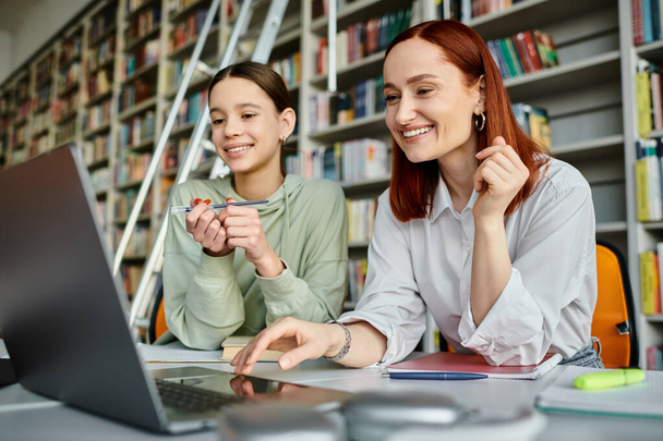 eine Tutorin und ihr Student arbeiten fleißig an einem Laptop in einer Bibliothek und engagieren sich in modernen Bildungspraktiken. - Foto, Bild