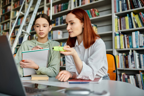 Teenager Mädchen und Tutor mit roten Haaren, engagieren sich in einer modernen Bildungsveranstaltung in einer Bibliothek, die sich auf einen Laptop-Bildschirm konzentriert. - Foto, Bild