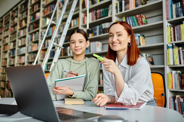 ένας δάσκαλος και ένα έφηβο κορίτσι, βυθισμένα στη σύγχρονη εκπαίδευση, χρησιμοποιώντας ένα φορητό υπολογιστή σε ένα άνετο περιβάλλον βιβλιοθήκη. - Φωτογραφία, εικόνα