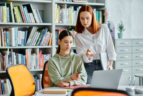 Duas mulheres, um tutor e um estudante, envolvidas em aulas pós-escolares em uma biblioteca, utilizando um laptop para a educação moderna. - Foto, Imagem