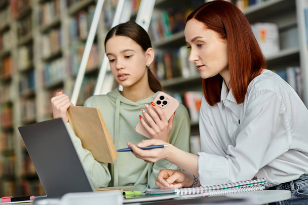 Репетитор с рыжими волосами учит девочку-подростка в библиотеке, используя ноутбук для современных образовательных ресурсов. - Фото, изображение