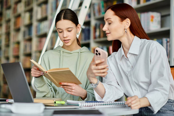 ένας κοκκινομάλλης δάσκαλος και μια έφηβη, κλεισμένοι σε ένα βιβλίο σε ένα τραπέζι βιβλιοθήκης, μαθαίνοντας μαζί. - Φωτογραφία, εικόνα